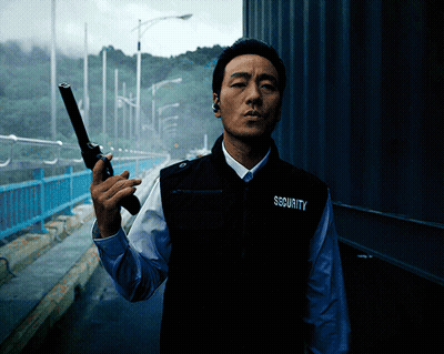 A Man Wearing A Vest That Says Security On It Holds A Gun GIF