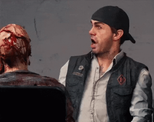 A Man Wearing A Vest With A Patch That Says ' Apocalypse ' On It Stands Next To A Bloody Statue GIF