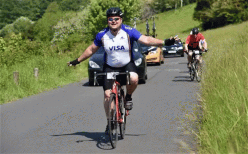 A Man Wearing A Visa Shirt Is Riding A Bike Down A Road GIF