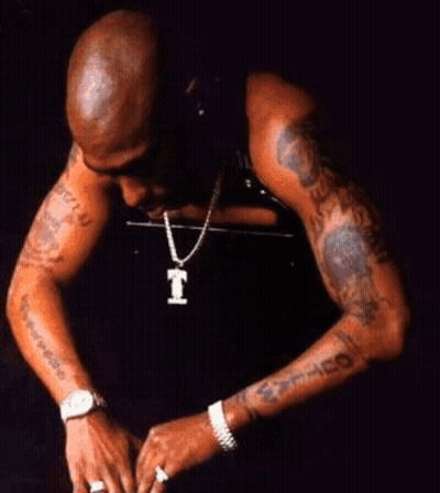 A Man Wearing A Watch And A Necklace With A Letter T On It GIF
