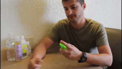 A Man Wearing A Watch Is Spraying Something On His Wrist While Sitting At A Table GIF