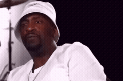 A Man Wearing A White Bucket Hat And A White Shirt Is Sitting In Front Of A Drum Set . GIF