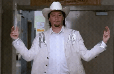 A Man Wearing A White Cowboy Hat And A White Jacket Is Standing In A Hallway With His Arms Outstretched . GIF