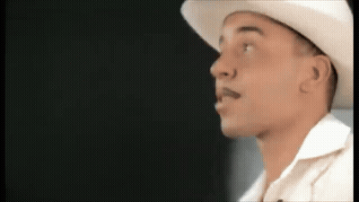 A Man Wearing A White Cowboy Hat And A White Shirt Is Looking To The Side . GIF