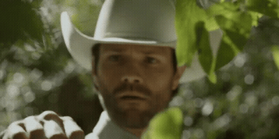 A Man Wearing A White Cowboy Hat And A White Shirt Is Standing In Front Of A Tree . GIF