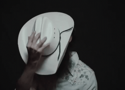 A Man Wearing A White Cowboy Hat Is Covering His Face With It GIF