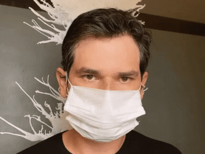 A Man Wearing A White Face Mask Stands In Front Of A Painting GIF