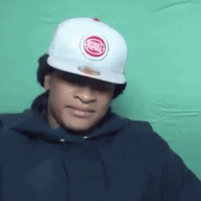 A Man Wearing A White Hat And A Black Hoodie Is Making A Face . GIF