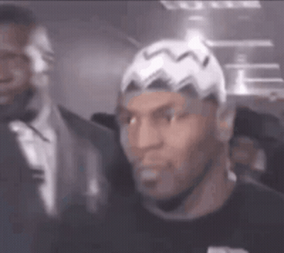 A Man Wearing A White Hat And A Black Shirt Is Standing Next To A Man In A Suit . GIF