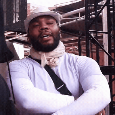 A Man Wearing A White Hat And A Scarf Around His Neck Is Standing With His Arms Crossed GIF
