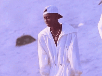 A Man Wearing A White Hat And A White Jacket Is Standing On The Beach . GIF