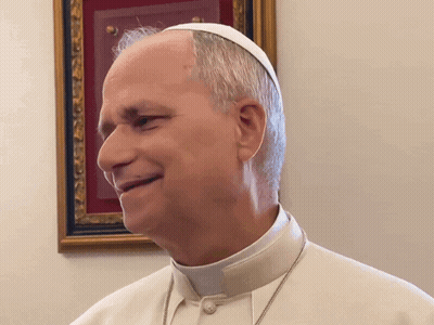 A Man Wearing A White Hat And Collar Is Smiling In Front Of A Framed Picture GIF