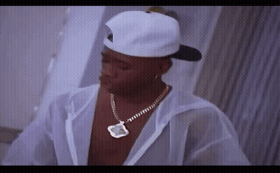 A Man Wearing A White Hat And Necklace Is Standing In A Room . GIF