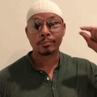 A Man Wearing A White Hat And Sunglasses Is Holding A Small Object In His Hand . GIF