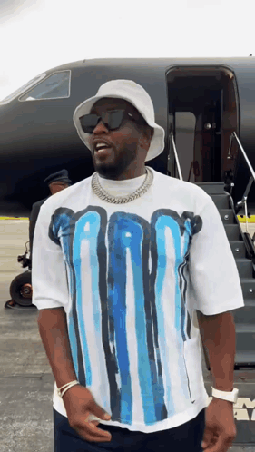 A Man Wearing A White Hat And Sunglasses Is Standing In Front Of A Plane GIF