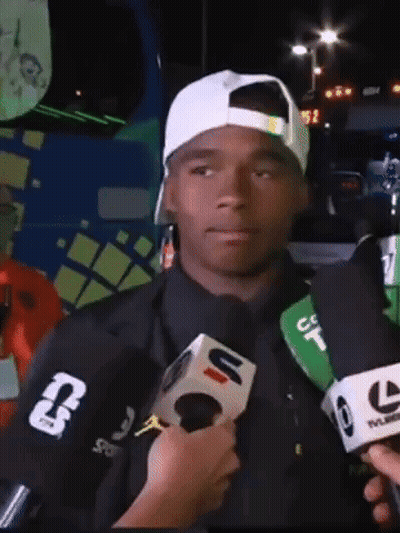 A Man Wearing A White Hat Is Being Interviewed By A Reporter Wearing A Jacket With The Letter T On The Sleeve GIF