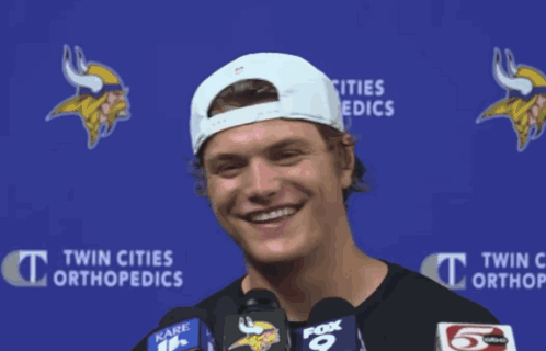 A Man Wearing A White Hat Is Smiling In Front Of A Blue Backdrop That Says Twin Cities Orthopedics GIF