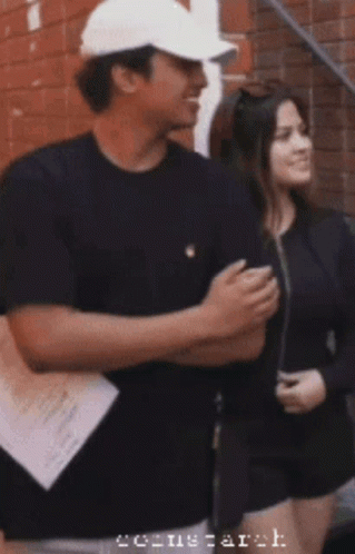 A Man Wearing A White Hat Is Standing Next To A Woman With The Word Arch On The Bottom Right GIF