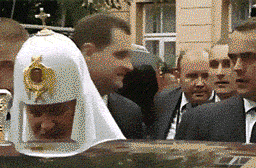 A Man Wearing A White Hat With A Cross On It Stands In A Crowd Of People GIF