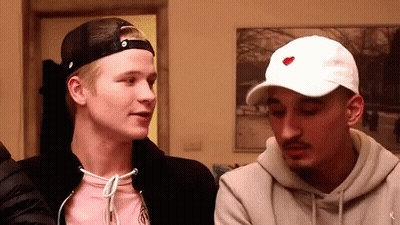 A Man Wearing A White Hat With A Red Heart On It Is Talking To Another Man . GIF