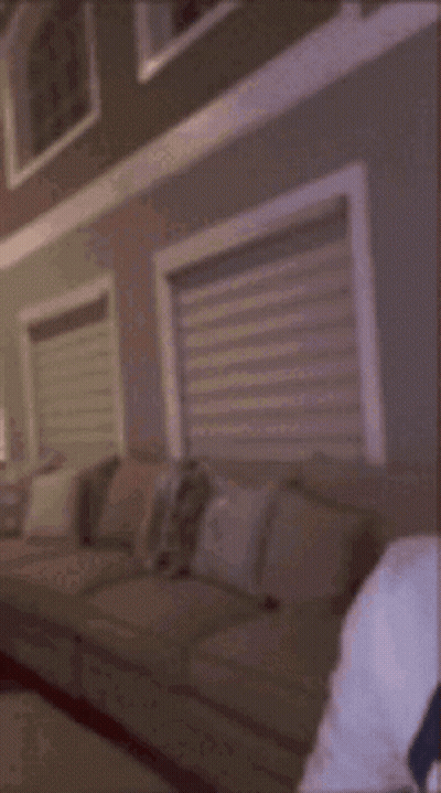 A Man Wearing A White Hoodie And Earbuds Is Sitting In Front Of A Window . GIF