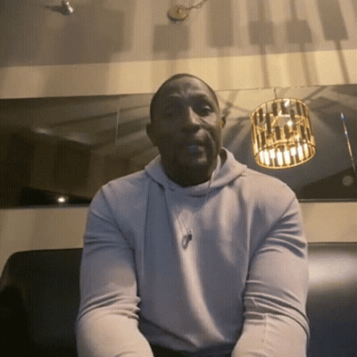 A Man Wearing A White Hoodie Sits On A Couch GIF