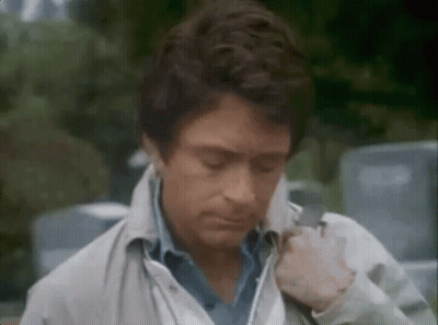 A Man Wearing A White Jacket And A Blue Shirt Is Standing In Front Of A Car . GIF