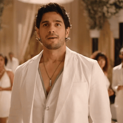 A Man Wearing A White Jacket And A Necklace Looks At The Camera GIF