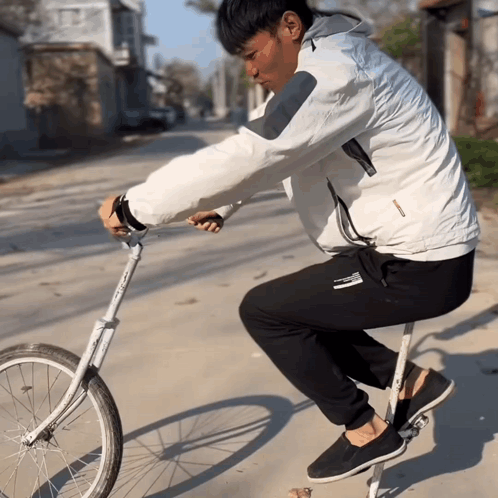 A Man Wearing A White Jacket And Black Pants Rides A Bicycle GIF
