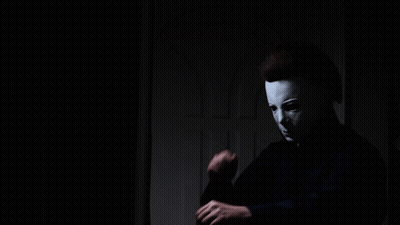 A Man Wearing A White Mask Is Standing In A Dark Room GIF