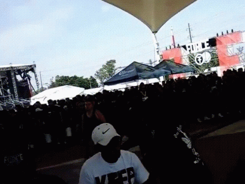 A Man Wearing A White Nike Hat Stands In Front Of A Crowd At A Music Festival GIF