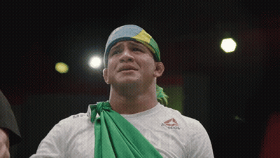 A Man Wearing A White Reebok Shirt With A Green Cloth Around His Neck GIF