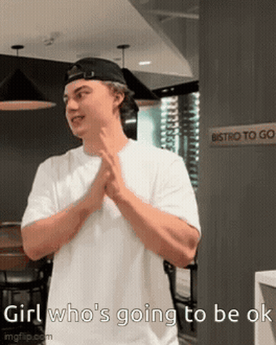 A Man Wearing A White Shirt And A Black Hat Is Standing In Front Of A Sign That Says Bistro To Go . GIF