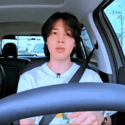 A Man Wearing A White Shirt And A Black Seat Belt Is Driving A Car GIF