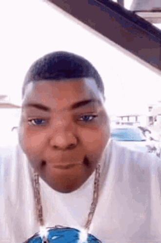 A Man Wearing A White Shirt And A Blue Necklace Is Making A Funny Face In A Car . GIF