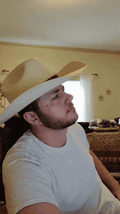 A Man Wearing A White Shirt And A Cowboy Hat Makes A Peace Sign GIF