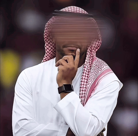 A Man Wearing A White Shirt And A Head Scarf Holds His Hand To His Chin GIF