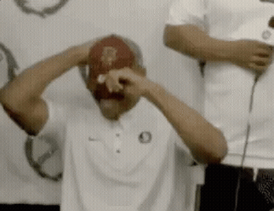 A Man Wearing A White Shirt And A Red Hat Is Holding His Head . GIF