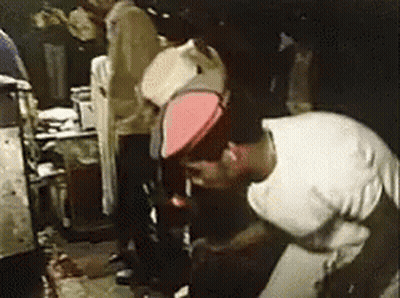 A Man Wearing A White Shirt And A Red Hat Is Kneeling Down In A Dark Room . GIF