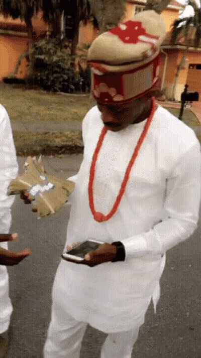 A Man Wearing A White Shirt And A Red Necklace Is Holding A Bunch Of Money GIF