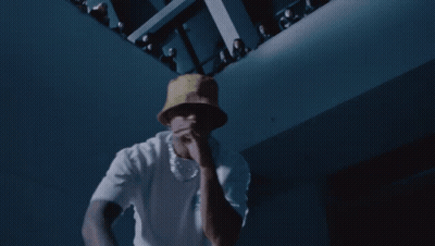 A Man Wearing A White Shirt And A Yellow Hat Is Dancing In A Dark Room GIF