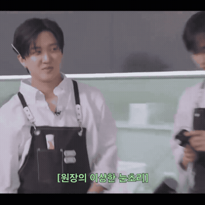 A Man Wearing A White Shirt And Black Apron Is Talking To Another Man GIF
