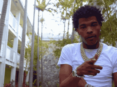 A Man Wearing A White Shirt And Gold Chains Is Standing In Front Of A Building GIF