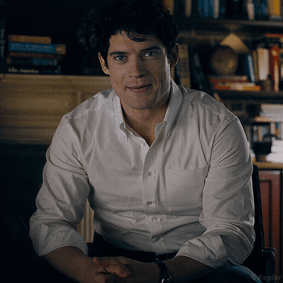 A Man Wearing A White Shirt Is Sitting In A Chair GIF