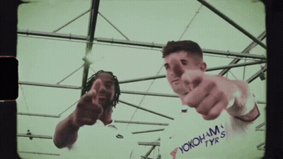 A Man Wearing A White Shirt That Says Yokohama Tyres Points At The Camera GIF