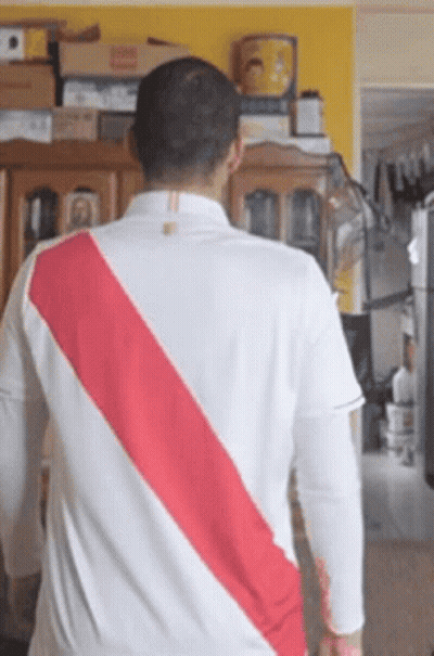 A Man Wearing A White Shirt With A Red Stripe On The Back Is Standing In A Living Room . GIF