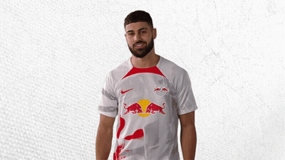 A Man Wearing A White Shirt With Red Bulls On It Is Waving GIF