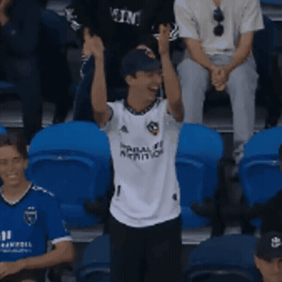 A Man Wearing A White Shirt With The Number 1 On It Stands In A Crowd GIF