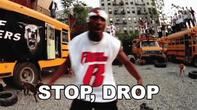 A Man Wearing A White Shirt With The Number 6 On It Is Standing In Front Of A Bunch Of School Buses And Says Stop Drop GIF