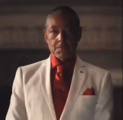 A Man Wearing A White Suit And Red Tie Is Looking At The Camera . GIF